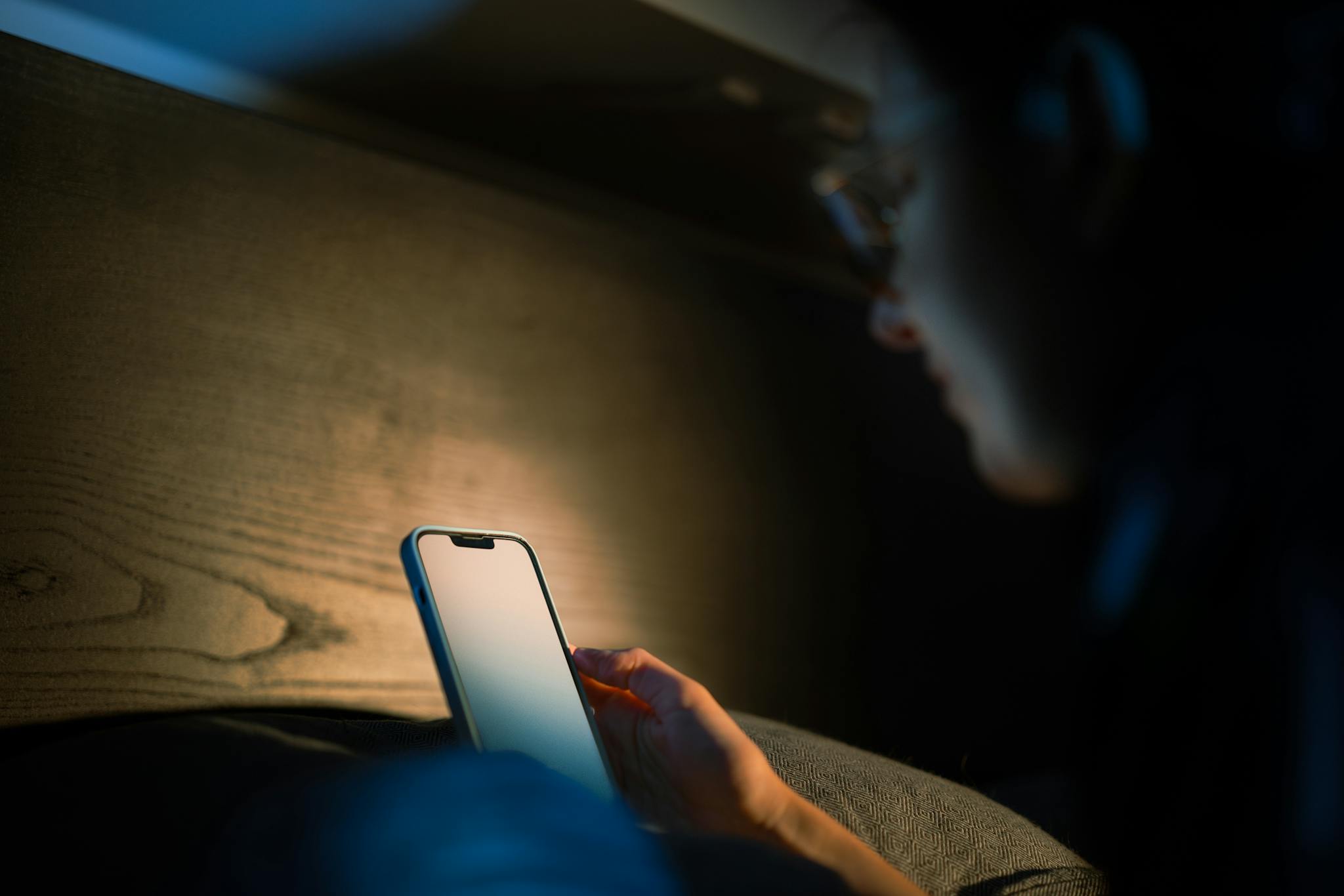 A person engages with a smartphone in a cozy, low light environment, suggesting a tech-savvy lifestyle.