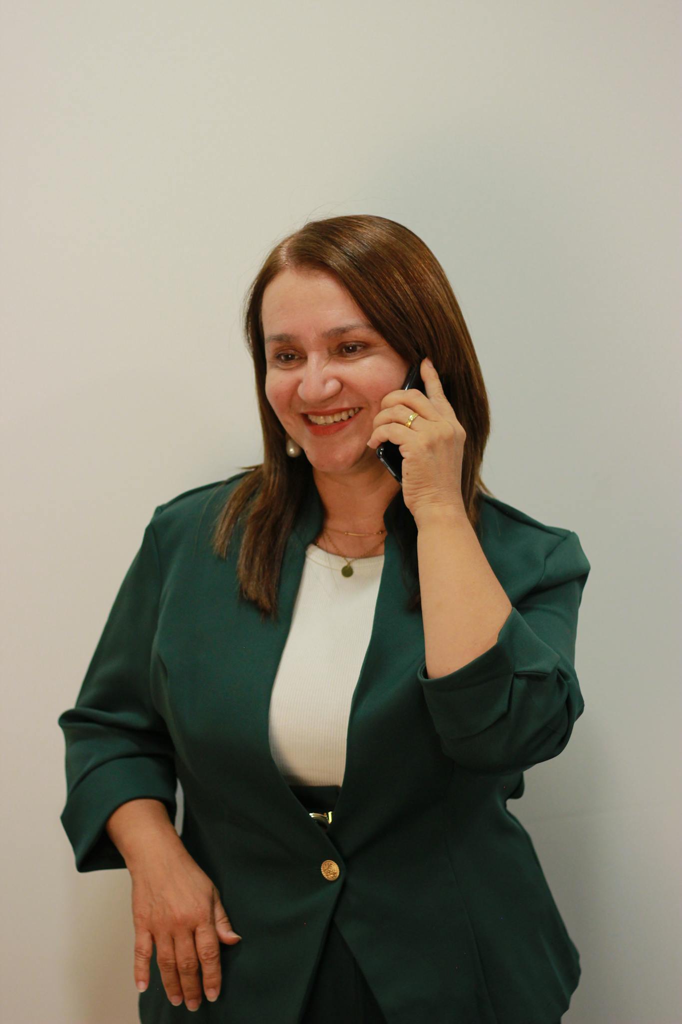 Smiling woman in green jacket on a phone call in a professional office setting.
